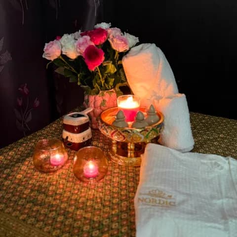 Kynttilöitä, ruusuja ja Nordic Thai Wellness -pyyhe hoitopöydällä
